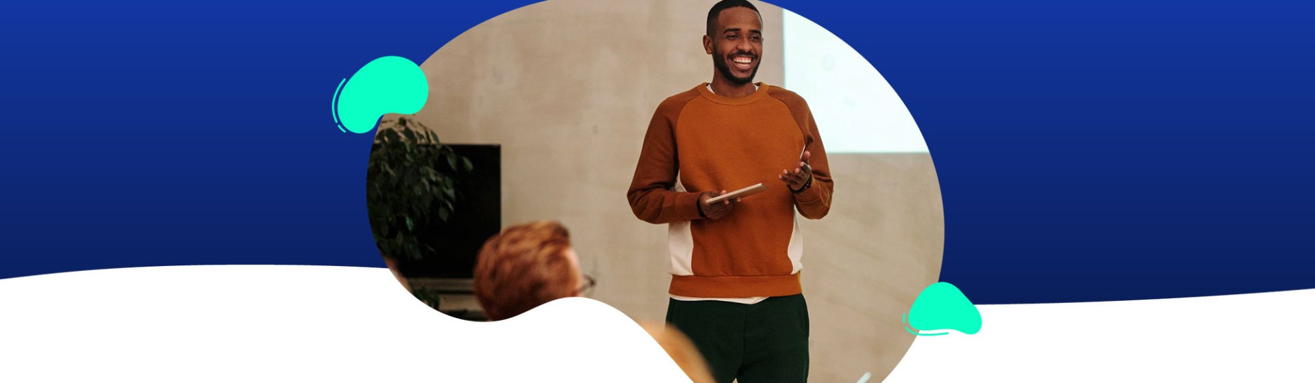 A person in an orange sweater is engaged in presentations, holding a tablet in front of a screen with an abstract blue and white background.