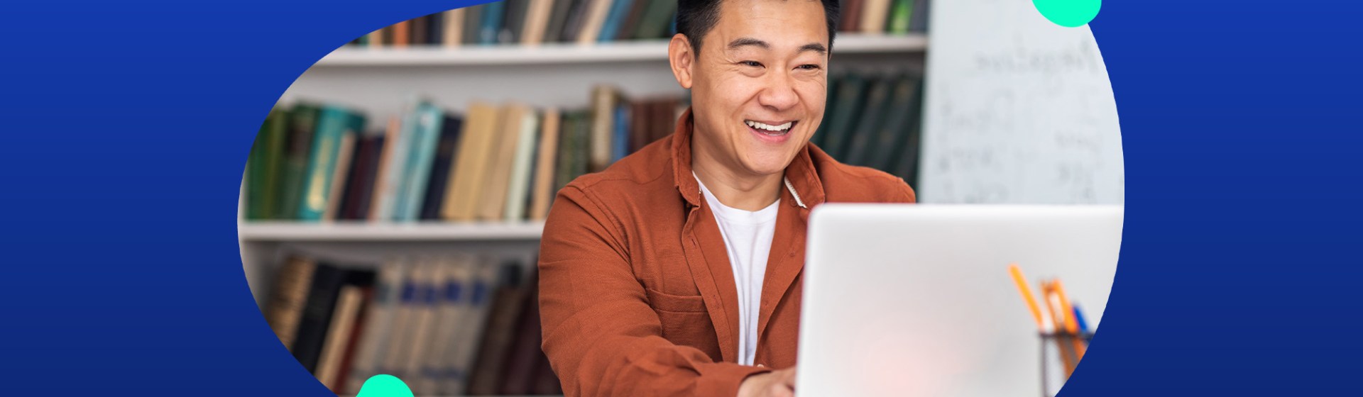A person in an orange shirt smiles while using a laptop in a library, preparing for the TeacherMatic Autumn Community Webinar. Bookshelves form the backdrop as they explore the latest updates and user AI insights.