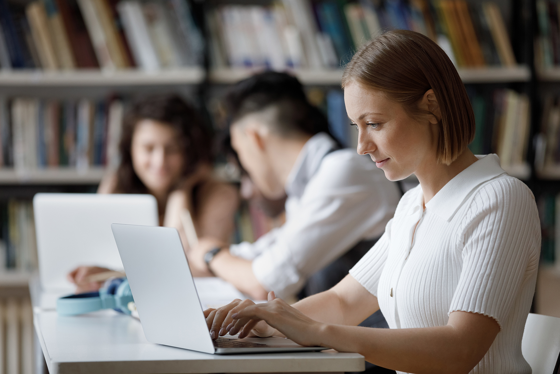 People sitting at a table in a library, working on laptops.