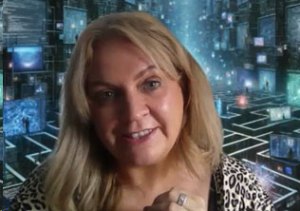 A person with long blonde hair is smiling in front of a futuristic digital background with multiple screens and lights.