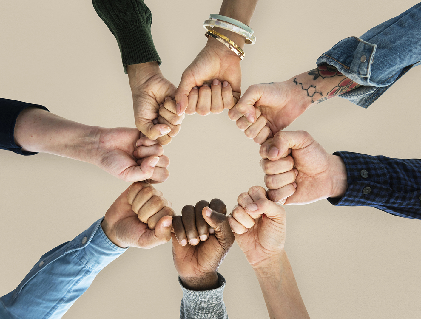 Eight hands of diverse individuals form a circle with their fists touching, viewed from above against a neutral background—symbolizing collaboration in curriculum design with TeacherMatic.