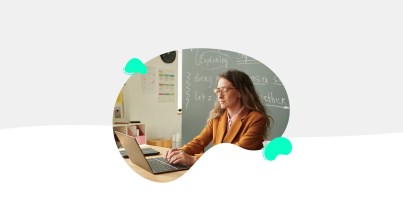 A person with long hair and glasses works on a laptop in a classroom, preparing for the TeacherMatic Autumn Community Webinar. In the background, a blackboard is filled with notes on the latest updates and user AI insights.