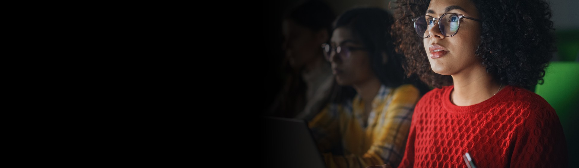 Focused individuals using laptops in a dimly lit room.
