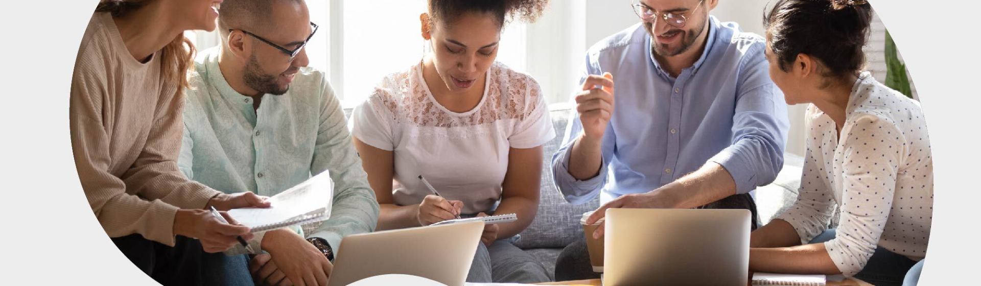 Five people are sitting around a table, engaged in discussion, with laptops and notebooks in front of them.